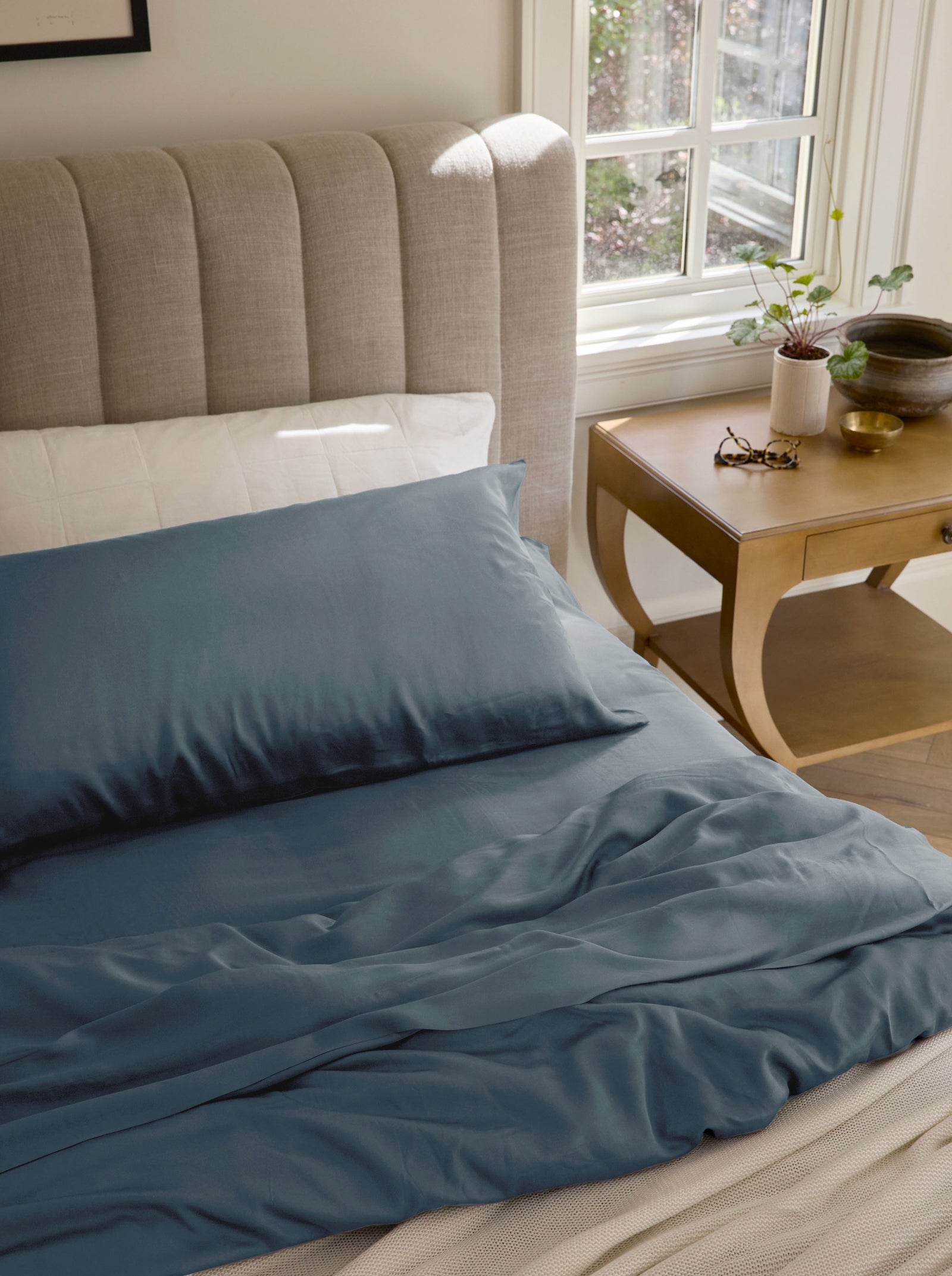 Pacific Blue bedding on an unmade bed with glasses on the nightstand 