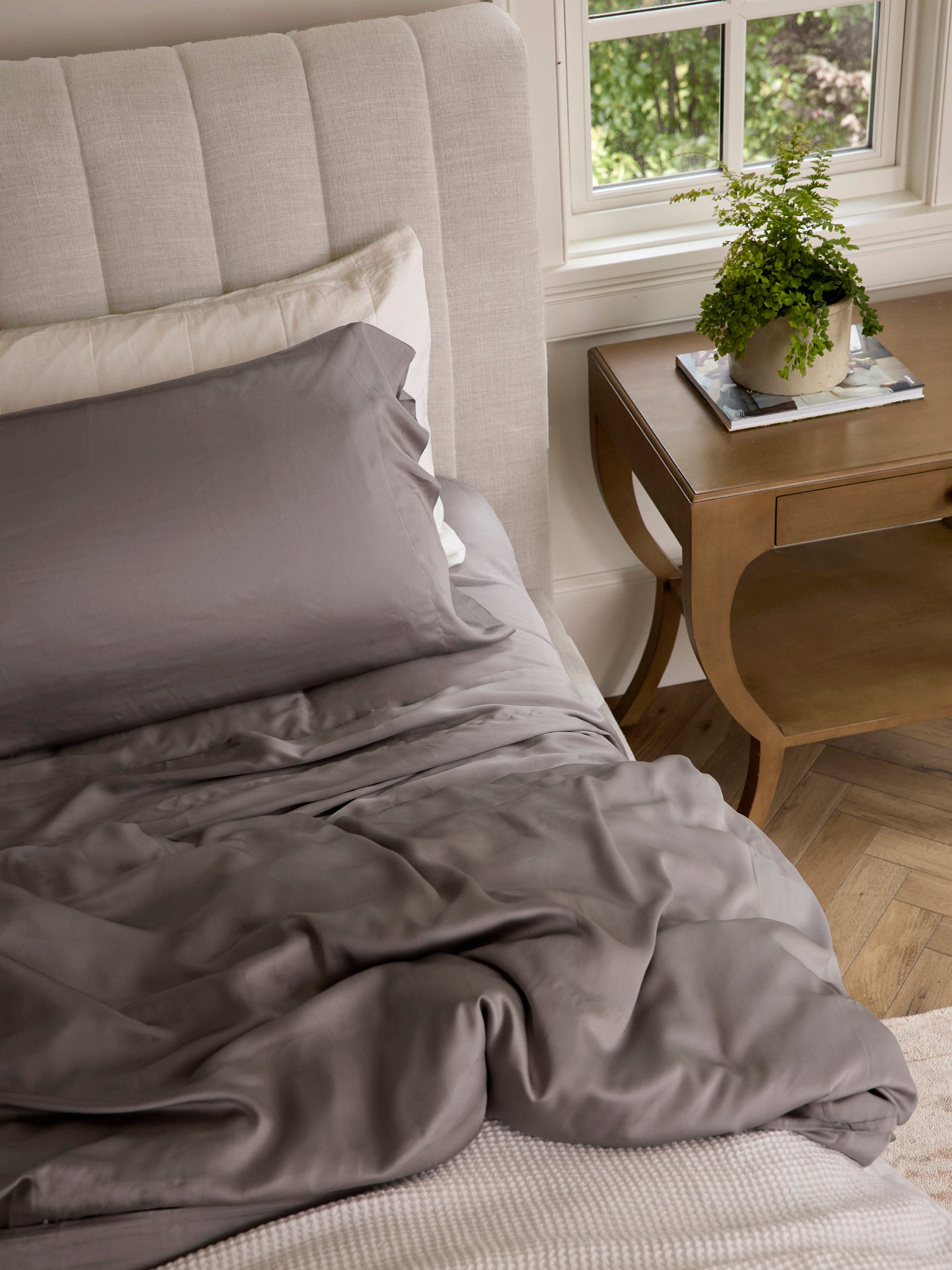 Stone bedding on an unmade bed with a plant on the nightstand 