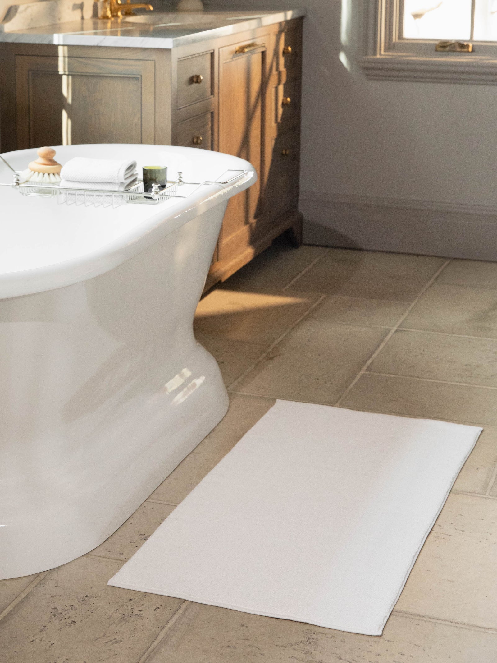 White looped terry bath mat resting on bathroom floor in front of bathtub. 