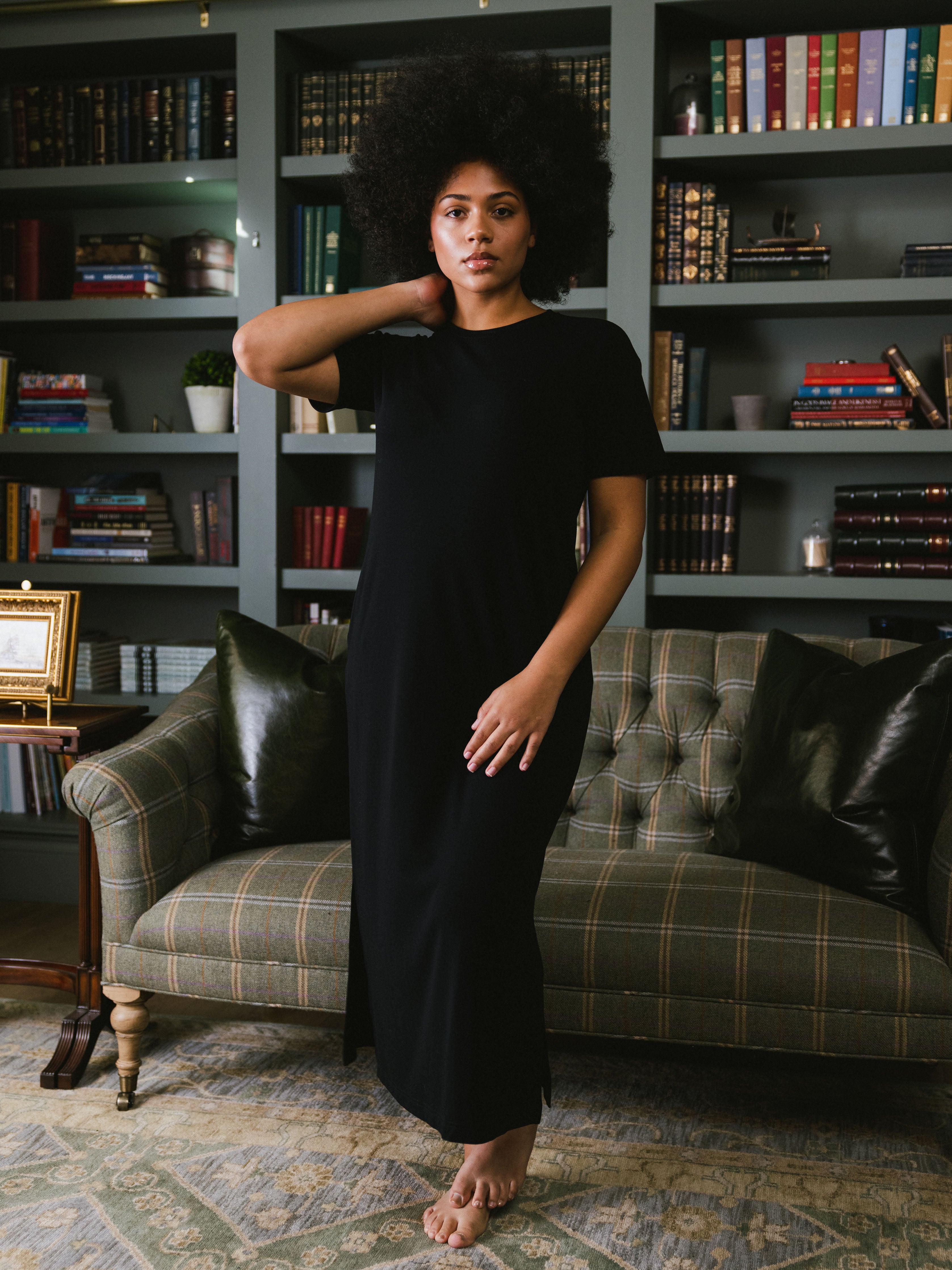 Black Bamboo Midi Dress modeled by a woman. The photo was taken in a living room setting, showing off the colors and lines of the dress. |Color: Black