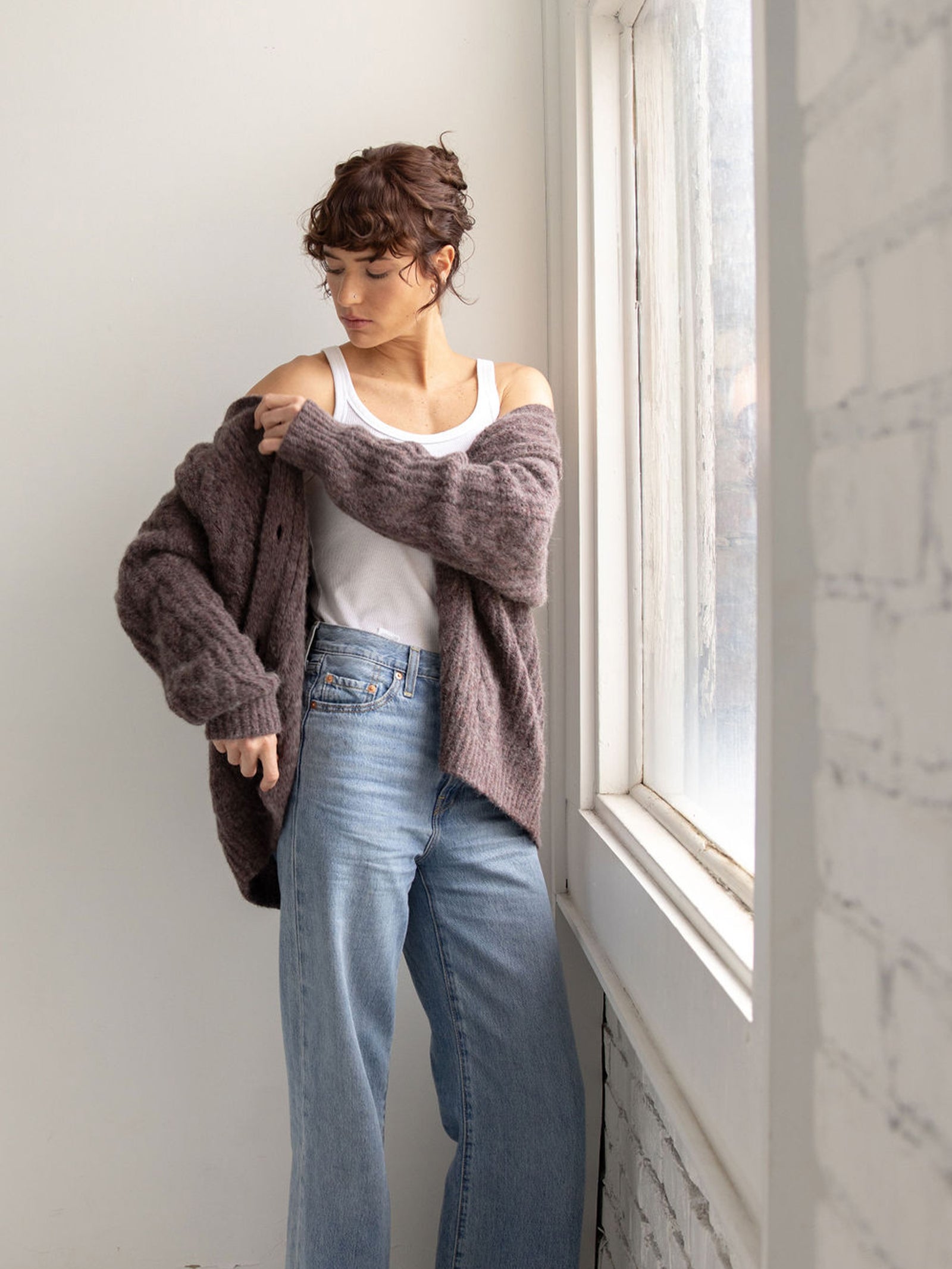 Woman in jeans and white tank with bordeaux cardigan over her arms 