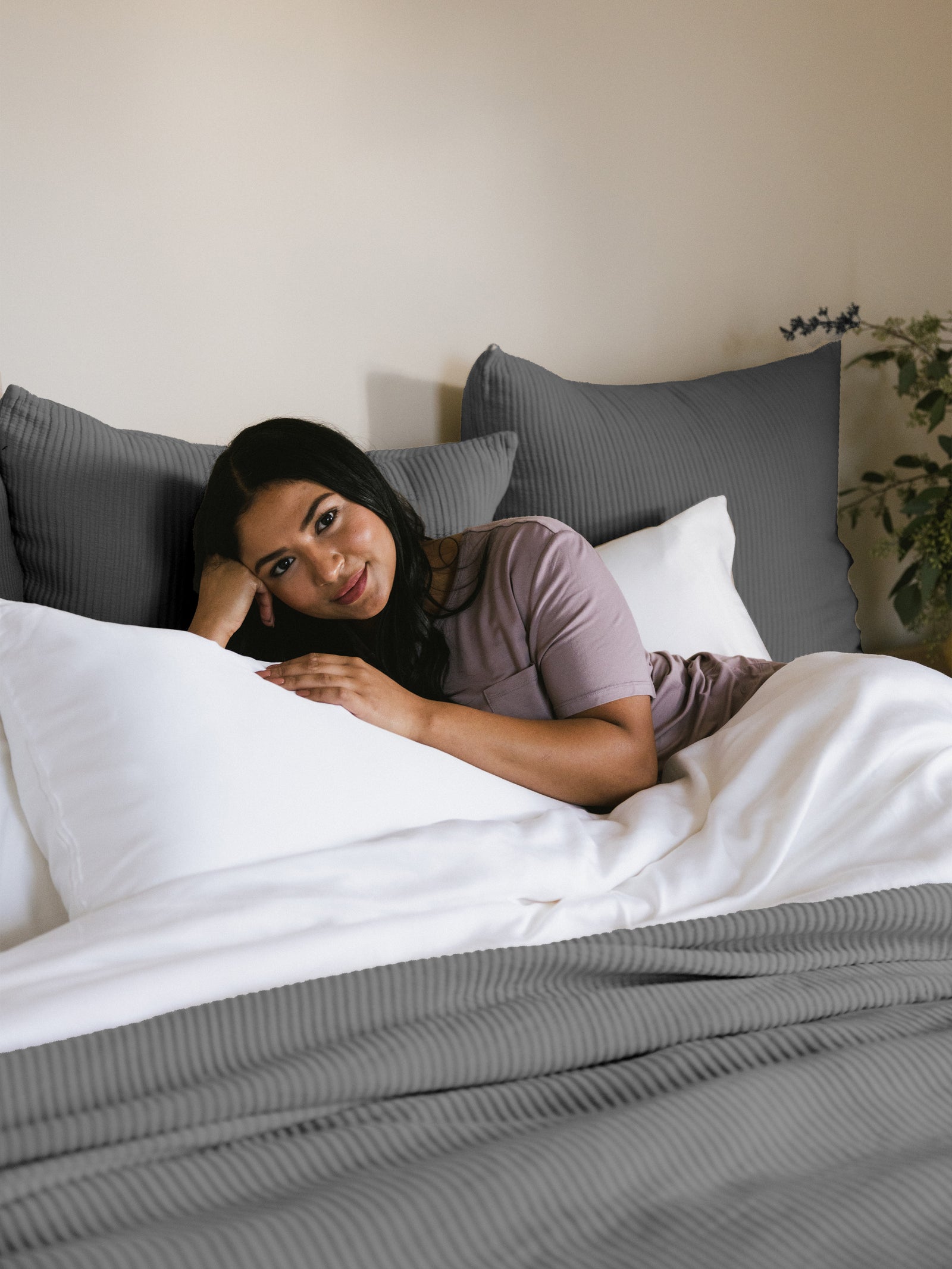 Woman laying in bed with charcoal shams and coverlet 