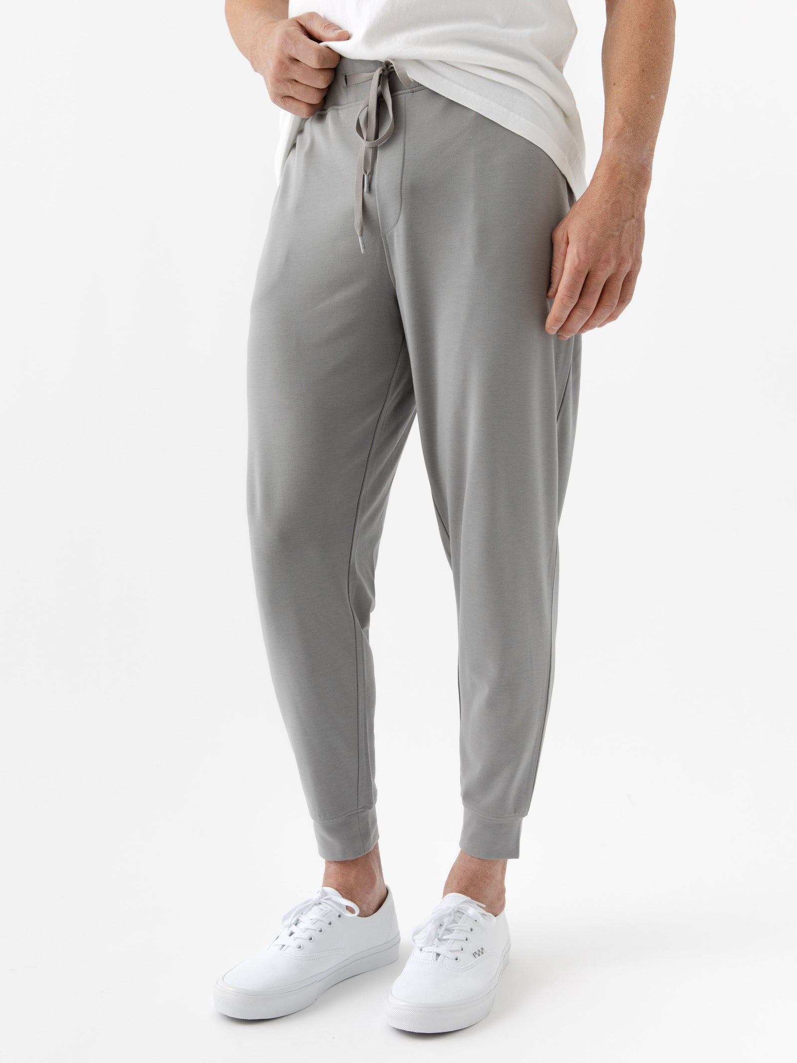 A person wearing Cozy Earth's Men's Bamboo Jogger Set in light gray, complemented by a white T-shirt and sneakers, against a plain white background. 
