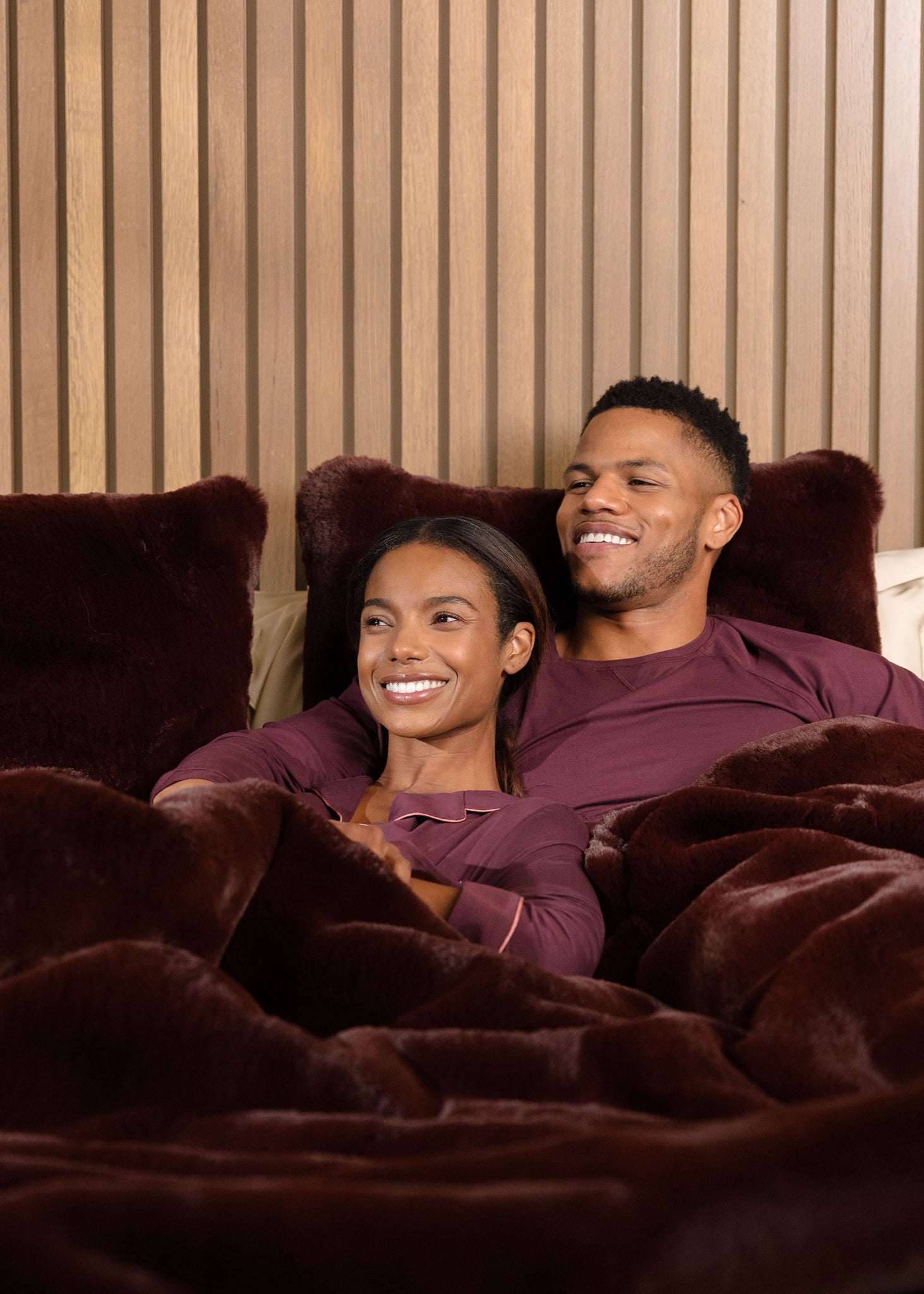 Couple laying in bed with burgundy oversized throw cuddle blanket and pillows 