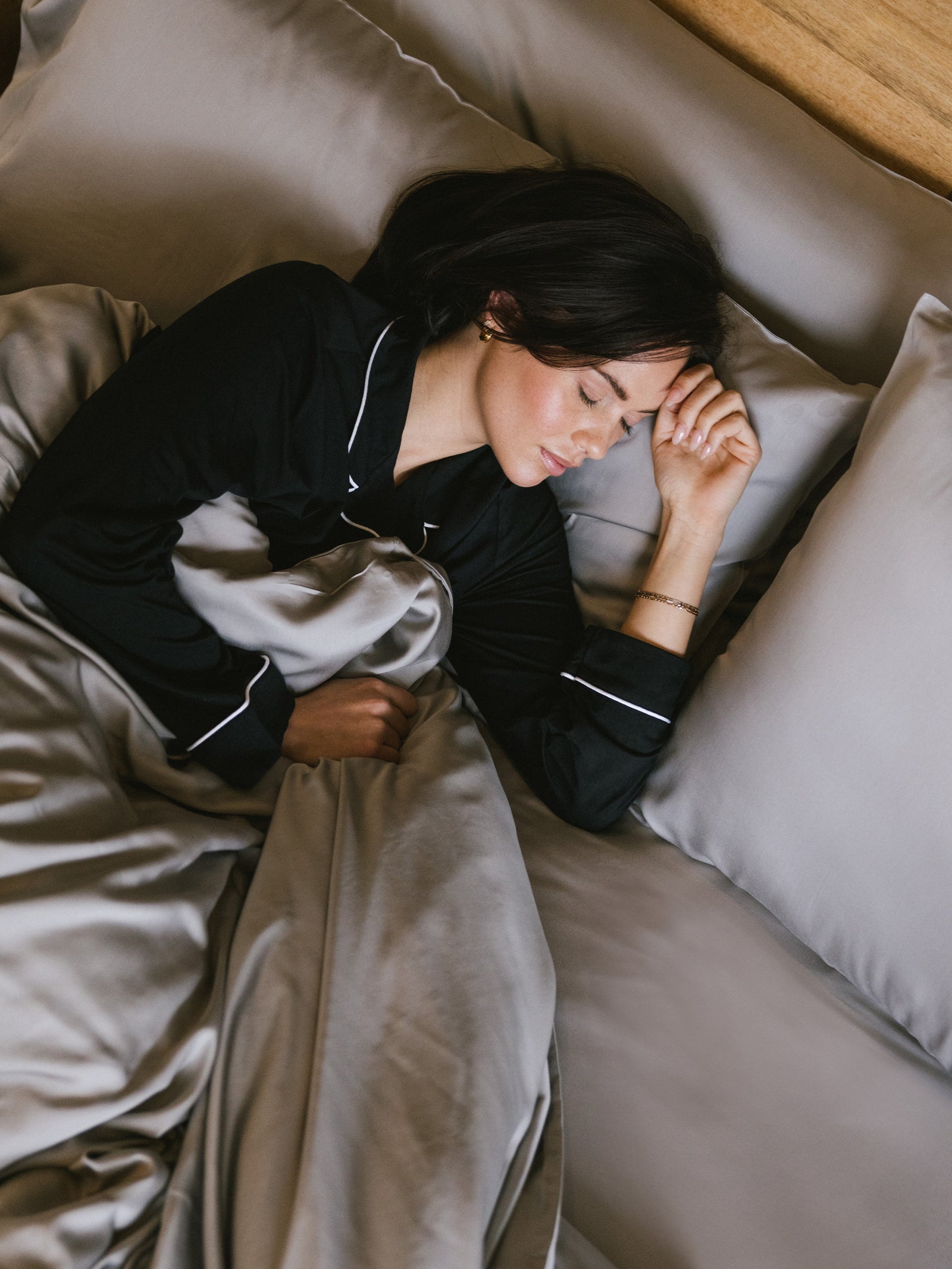 Woman in black pajamas sleeping in bed with dove grey bedding 