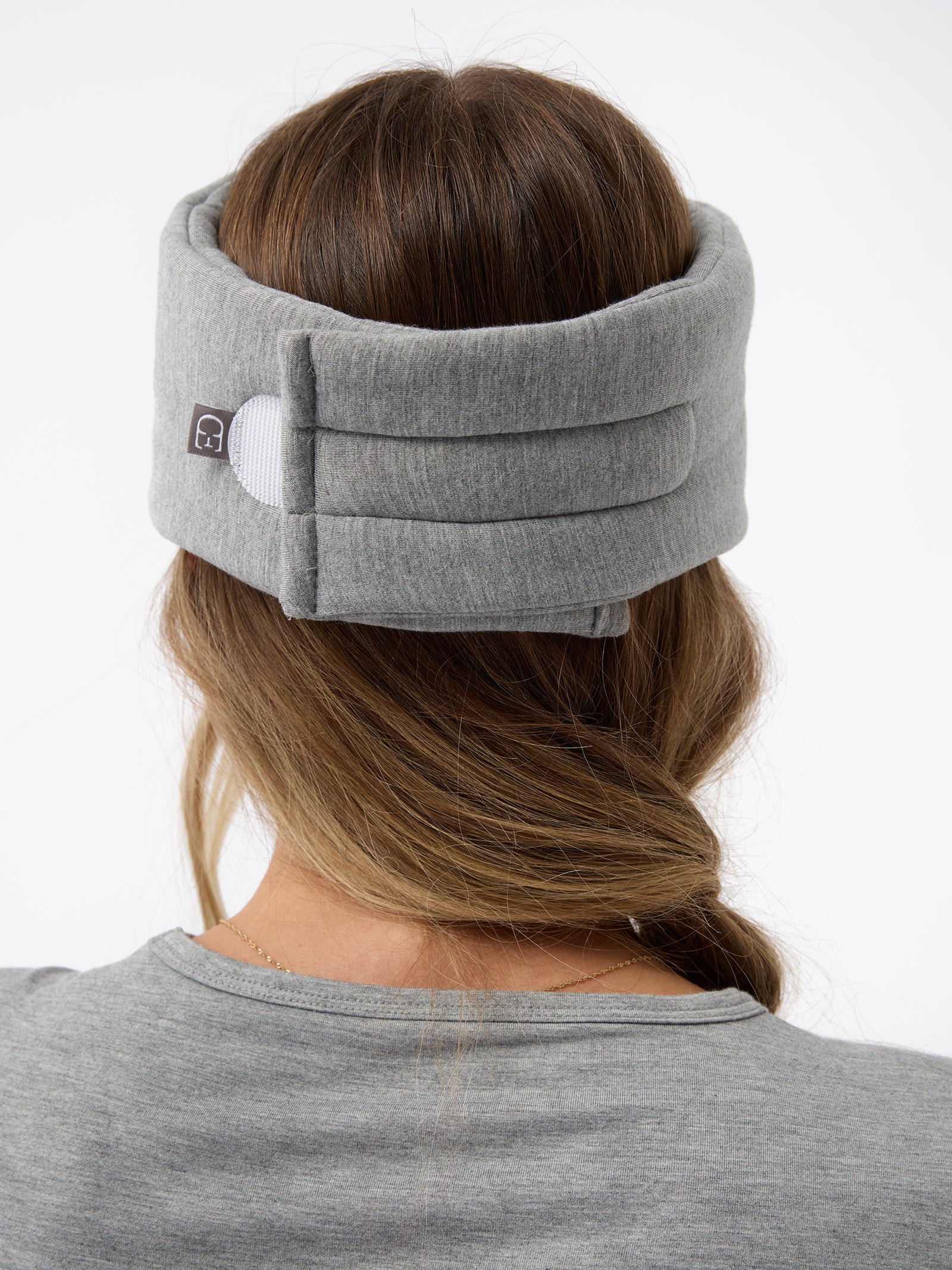 A woman wears the Cozy Earth Adjustable Bamboo Sleep Mask in Grey. She is facing away and showing where the mask fastens at the back. 