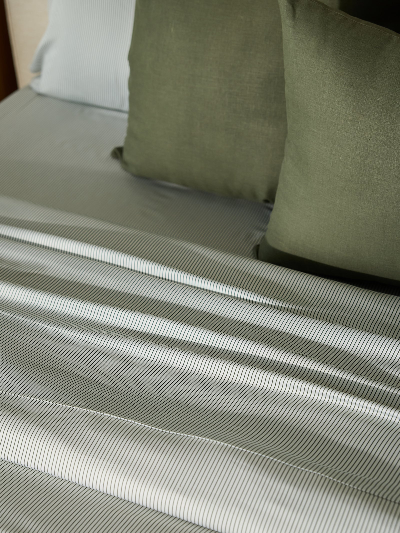 A neatly made bed featuring the Cozy Earth Bamboo Duvet Cover in shades of gray. Green square pillows are arranged on the bed, adding a touch of color. The smooth and polished fabric creates an inviting and cozy atmosphere. 