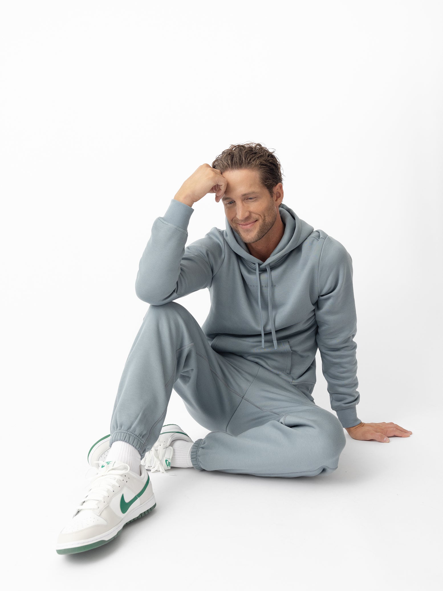 Man sitting on ground wearing smokey blue cityscape hoodie and sweats 