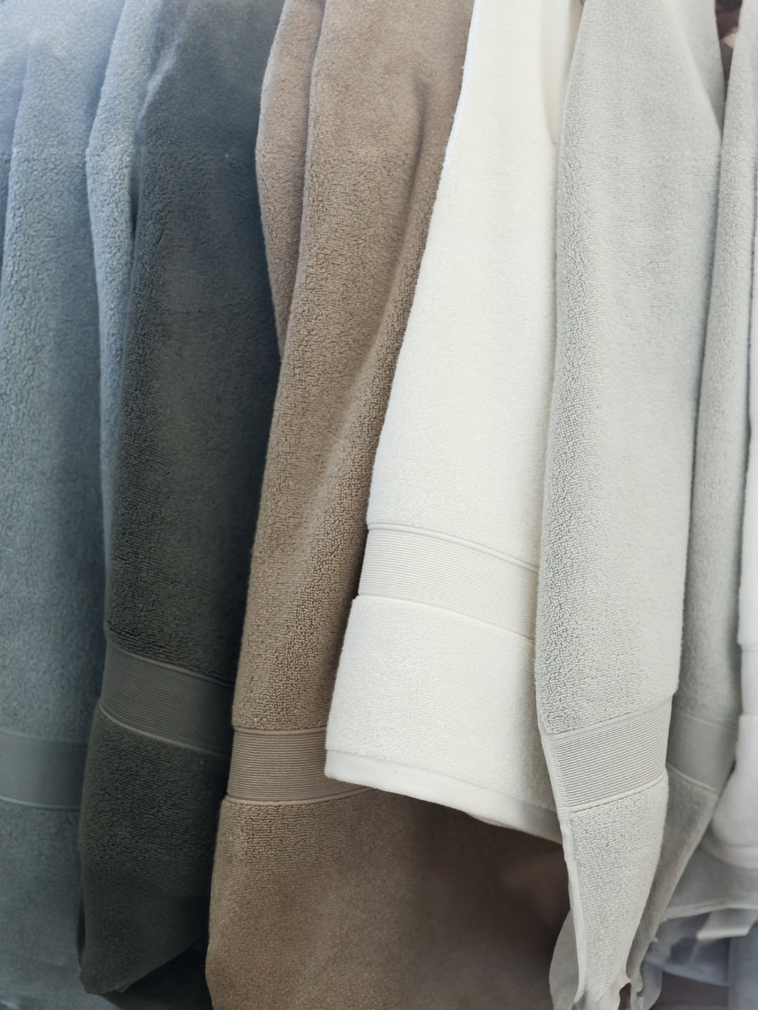 Light grey, seashell, white, sand, charcoal, and harbor mist luxe bath towels hanging side by side