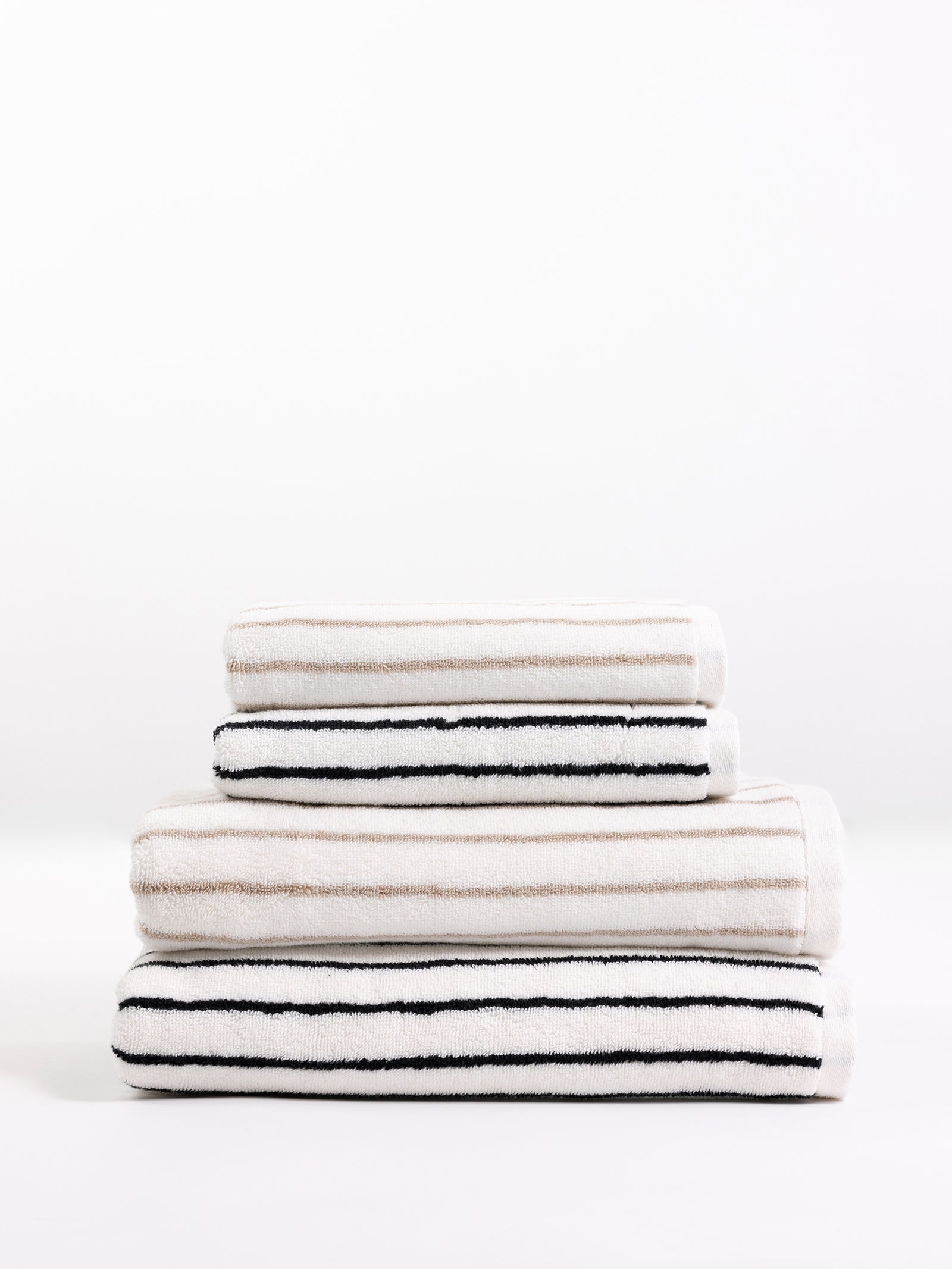 A neatly folded stack of three Luxe Hand Towels by Cozy Earth sits elegantly. The towels feature alternating horizontal black and white stripes in a minimalist design. The stack is arranged from the largest at the bottom to the smallest at the top, set against a plain white background. 