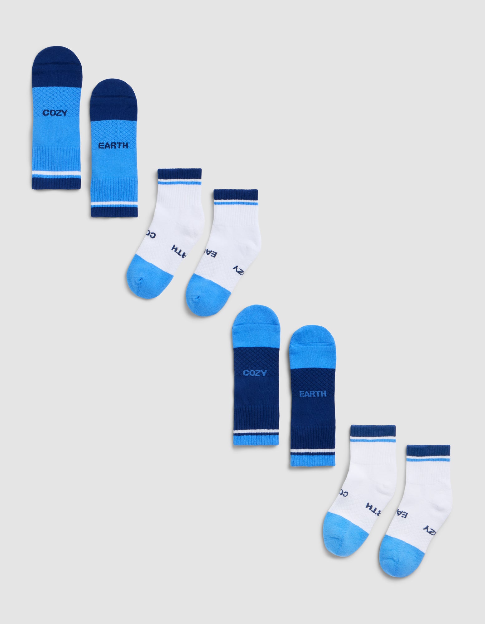Four pairs of children’s socks from Cozy Earth’s Essential Quarter Sock 4-Pack are arranged diagonally on a light gray background, featuring white and blue colors with "COZY" and "EARTH" written on them. 