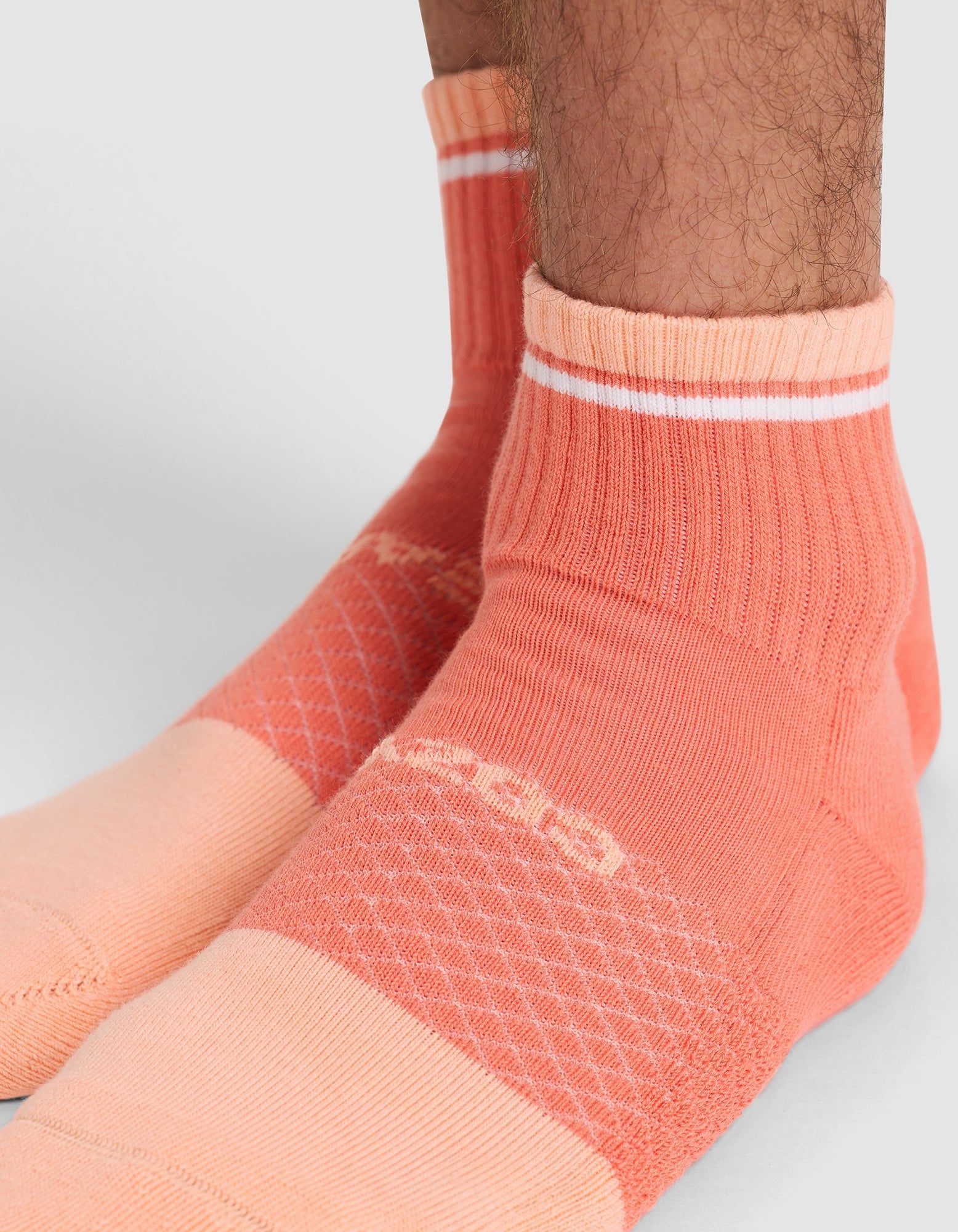 Close-up of a person's lower legs and feet wearing Cozy Earth's Essential Quarter Sock in peach and coral with white stripes. The sock features ribbed ankles and a patterned knit design on the foot. 