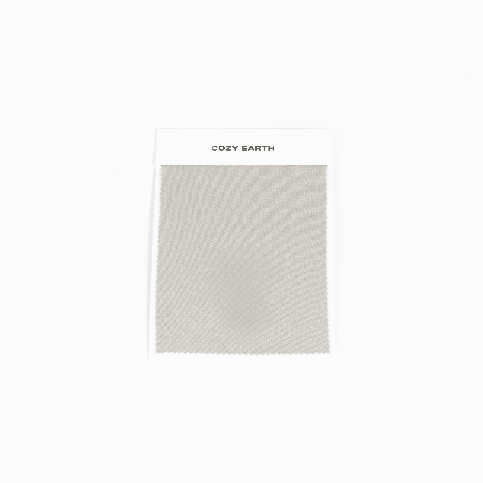 A "Bamboo Sheet Swatch" from Cozy Earth, featuring a light gray fabric with a smooth texture and a zigzag edge, displayed against a white background. 