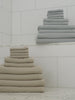 Harbor Mist and Sand colored waffle bath bundles rest on a marble floor in a shower room. Close ups of the towels can be seen