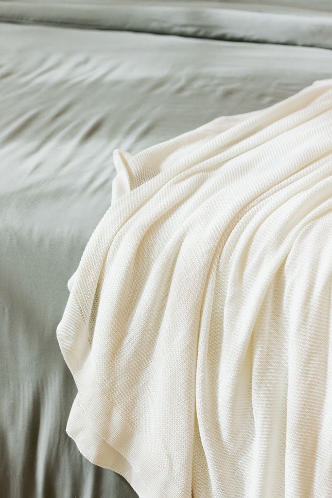 Ivory cloud knit blanket sitting on bed |Color:Ivory