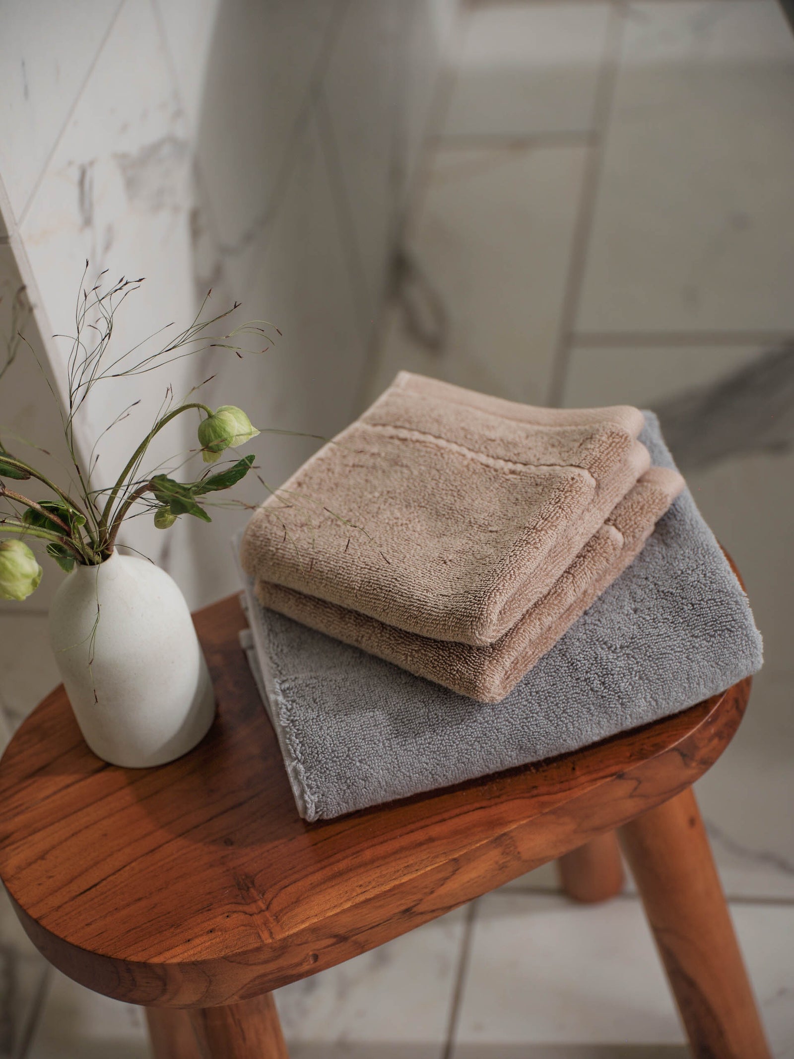 Premium Plush Hand Towels in the color Sand and Harbor Mist. Photo of Sand and Harbor Mist Premium Plush Hand Towels taken resting on a stool in a bathroom with marble tile.