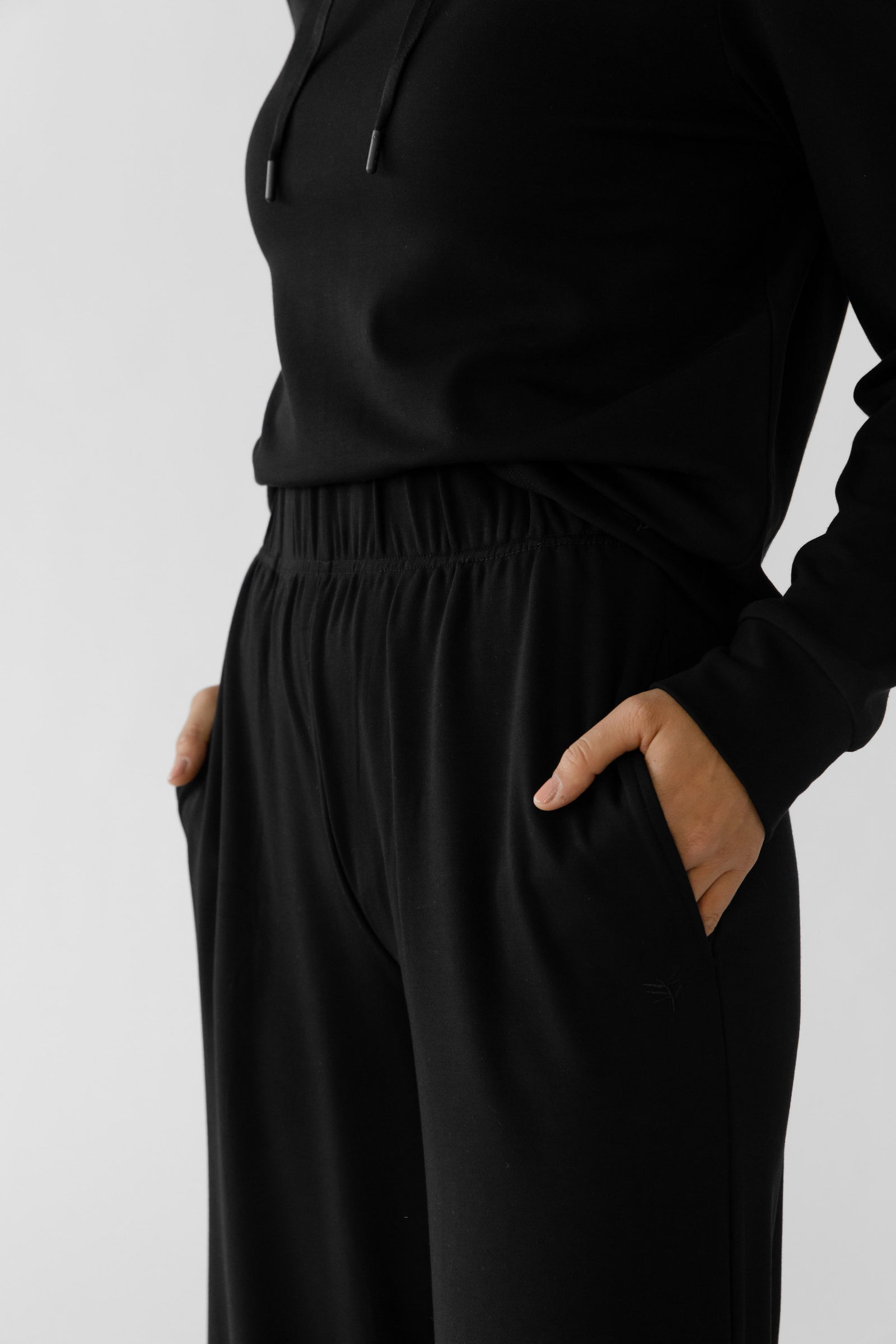 A person wearing Cozy Earth's Women's Ultra-Soft Bamboo Wide Leg Pull On Pant TALL in black, with their hand in the pocket, standing against a plain white background. 