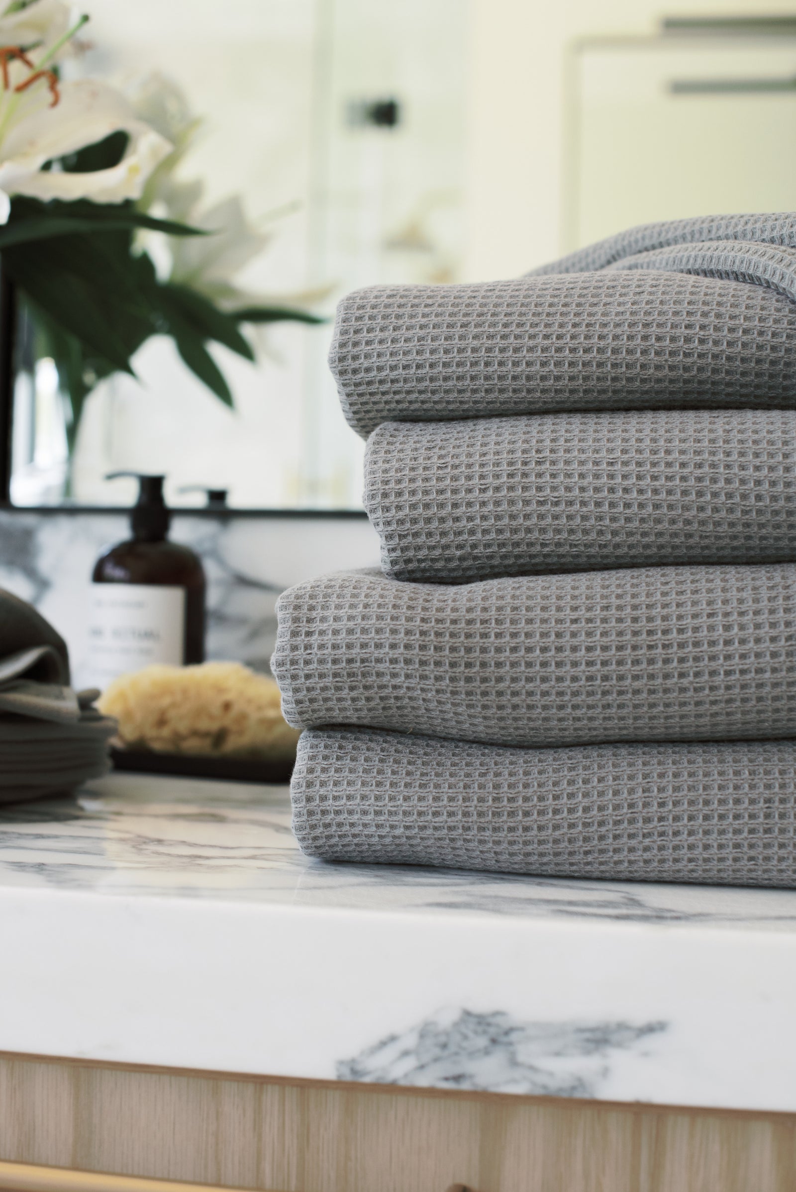 Waffle Bath Towel in the color Charcoal. Photo of Charcoal Waffle Bath Towel taken with Charcoal Waffle Bath Towel resting on a bathroom sink. 